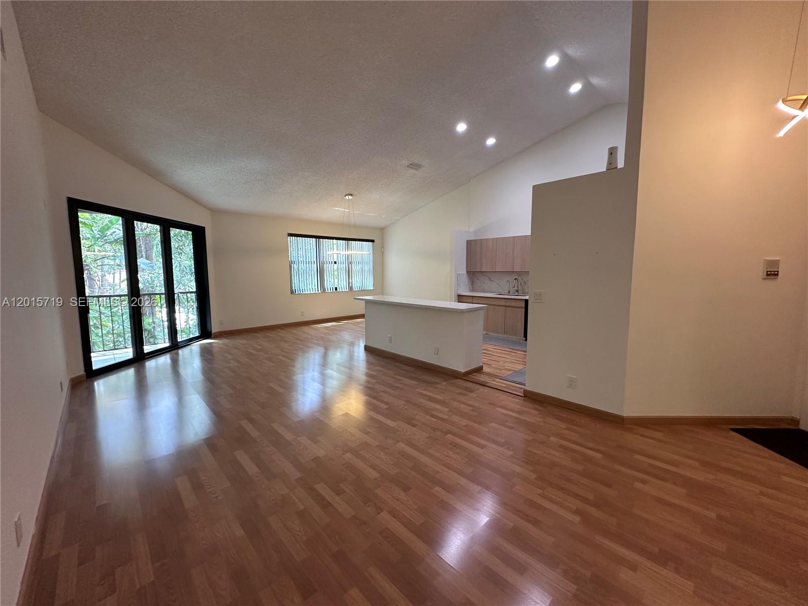 An open-concept living area features wood flooring, a kitchen island, and sliding glass balcony doors — 5790 Coach House Cir, Boca Raton FL 33486, BOCA RATON, FL