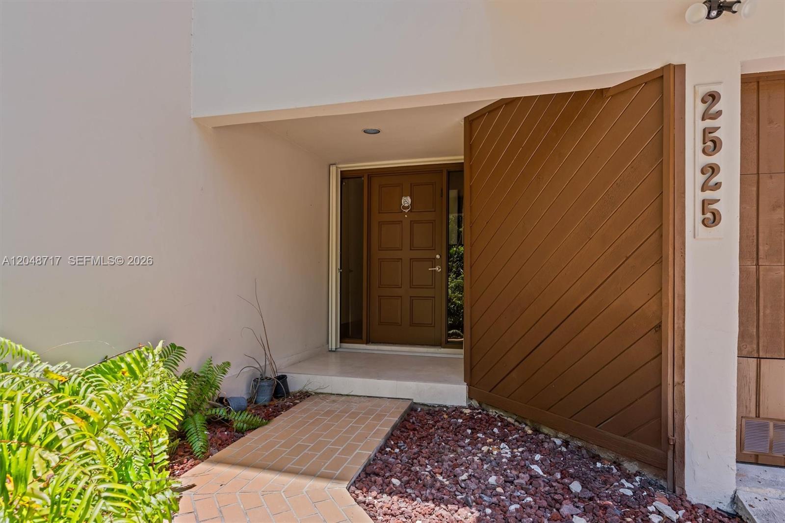 The exterior entrance features a brown door, diagonal wood siding, and a brick walkway — 2525 NE 135th St, North Miami FL 33181, NORTH MIAMI, FL