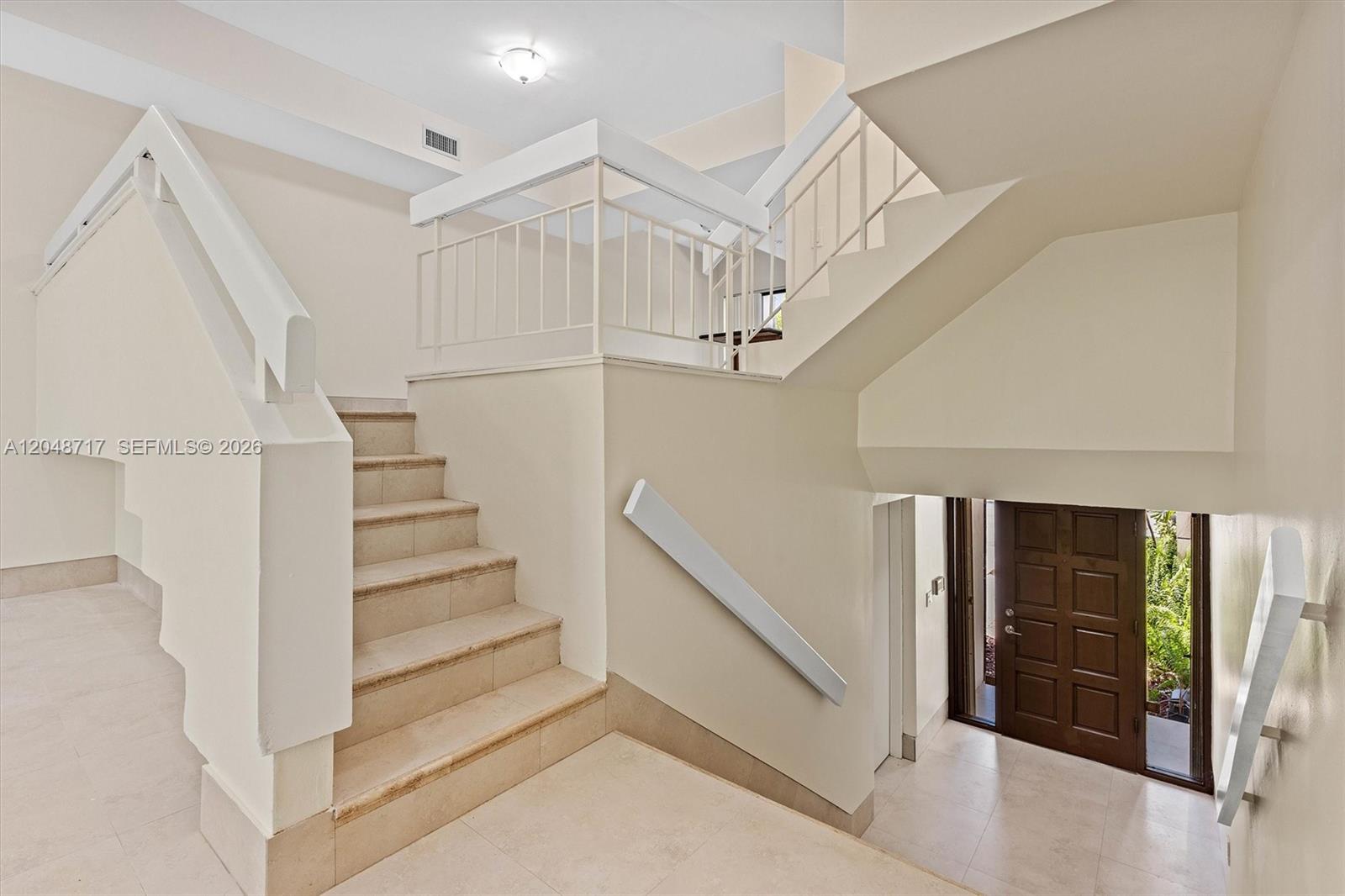 An interior view shows a tiled staircase leading to an upper landing with white railings — 2525 NE 135th St, North Miami FL 33181, NORTH MIAMI, FL
