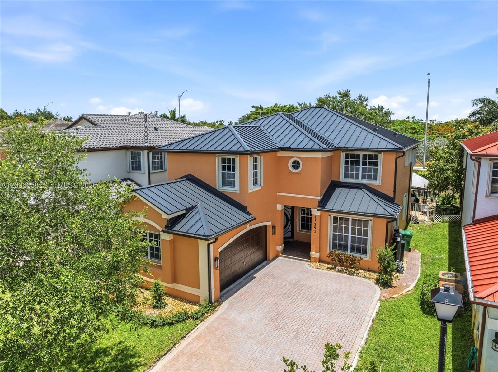 An orange two-story house features a dark metal roof, a garage, and a paved driveway — 15391 SW 18th St, Miramar FL 33027, MIRAMAR, FL