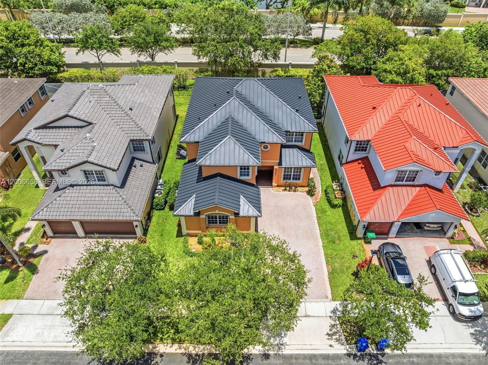 An aerial view shows three suburban houses with different colored metal and tile roofs — 15391 SW 18th St, Miramar FL 33027, MIRAMAR, FL
