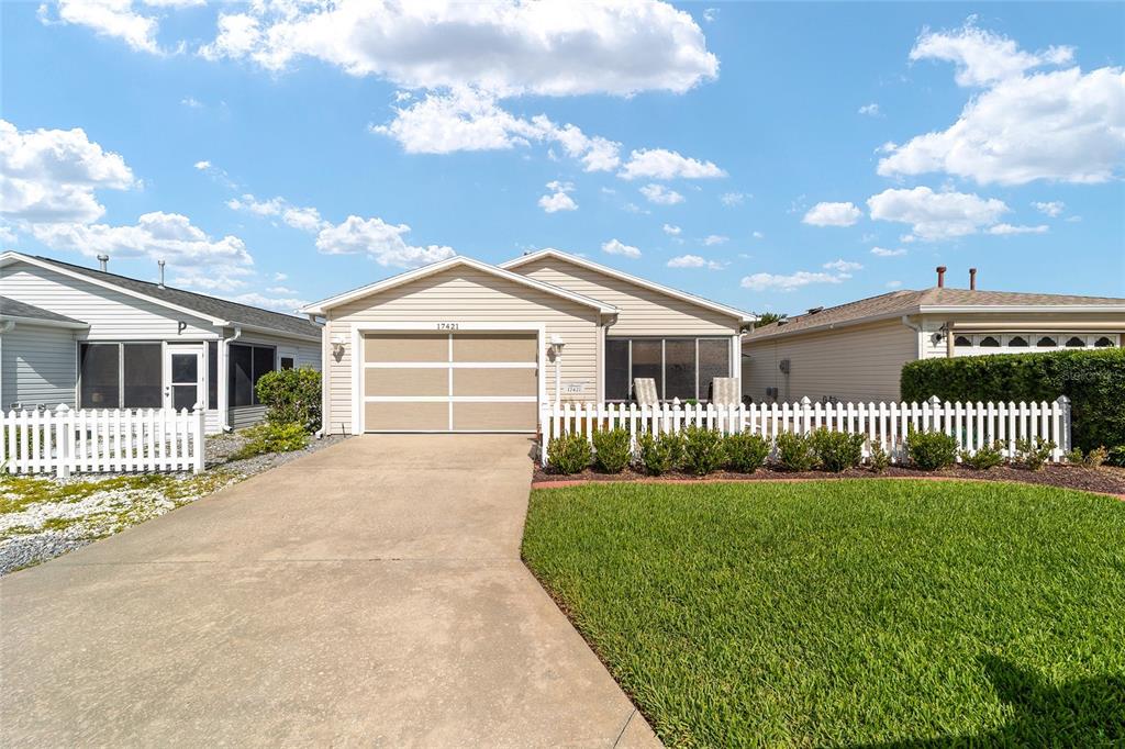 A single-story house with beige siding, a two-car garage, and a white picket fence — 17421 SE 78TH HARMONY CIRCLE, THE VILLAGES, FL