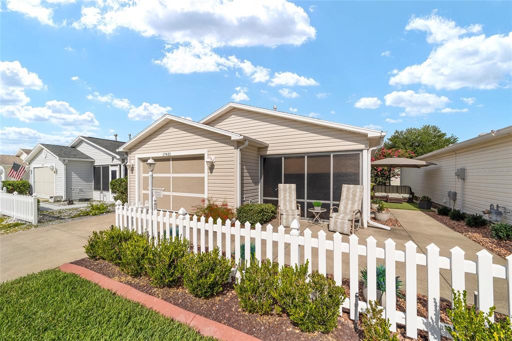 A single-story house with beige siding, a white picket fence, and a screened-in front porch — 17421 SE 78TH HARMONY CIRCLE, THE VILLAGES, FL