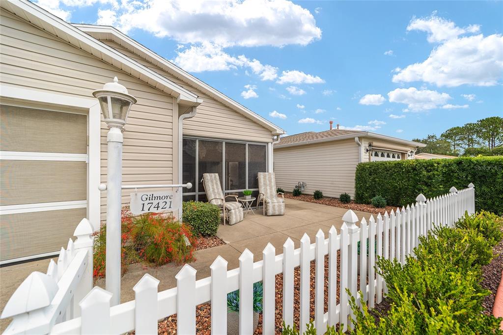 A white picket fence encloses a concrete patio with two chairs beside a house exterior — 17421 SE 78TH HARMONY CIRCLE, THE VILLAGES, FL