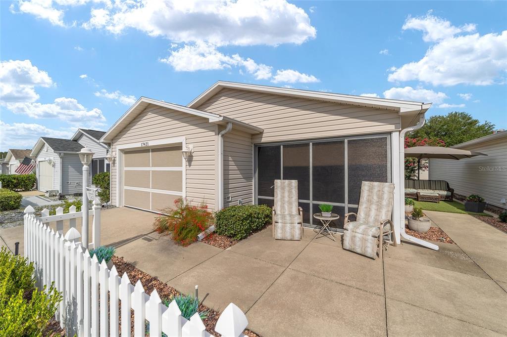 A beige house features a screened-in front porch, a garage, and a white picket fence — 17421 SE 78TH HARMONY CIRCLE, THE VILLAGES, FL
