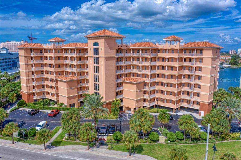 An exterior view of a multi-story, peach-colored apartment building with balconies and a parking lot — 530 S GULFVIEW BOULEVARD UNIT 401, CLEARWATER BEACH, FL