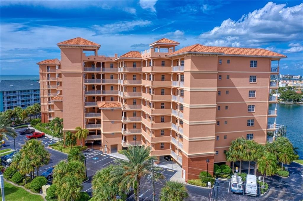 An aerial view of a multi-story, peach-colored apartment building with balconies and a parking lot — 530 S GULFVIEW BOULEVARD UNIT 401, CLEARWATER BEACH, FL