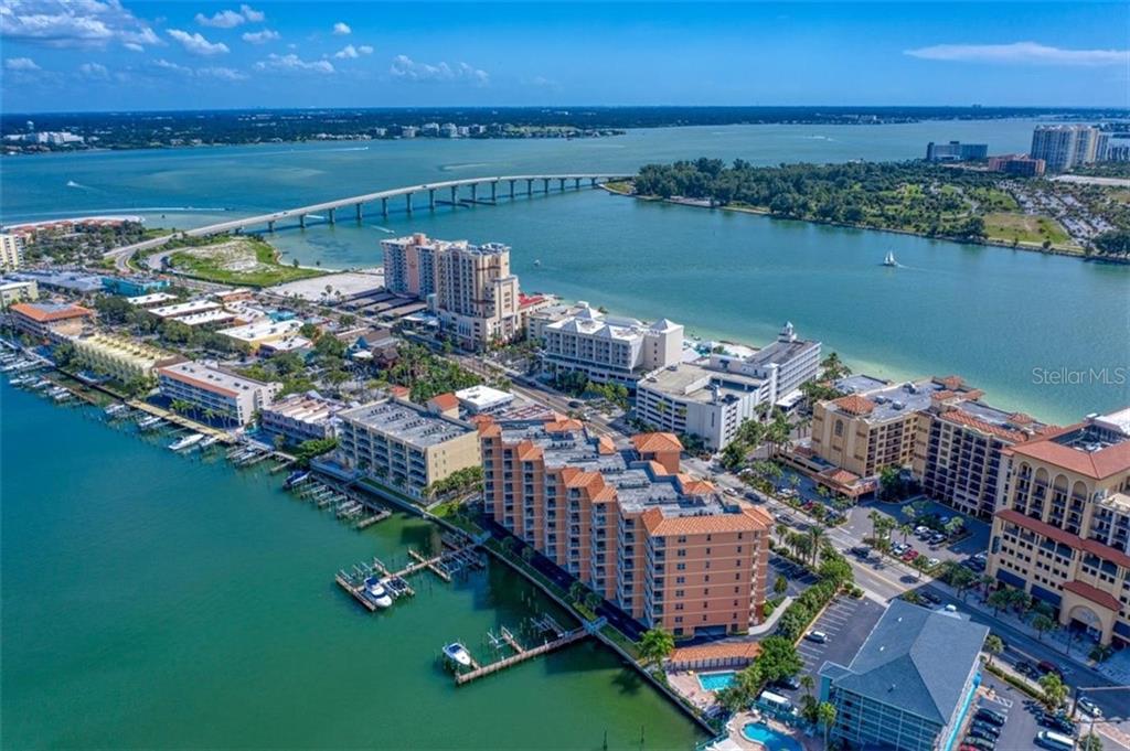 An aerial view shows a coastal resort complex with multi-story buildings, boat docks, and a bridge — 530 S GULFVIEW BOULEVARD UNIT 401, CLEARWATER BEACH, FL