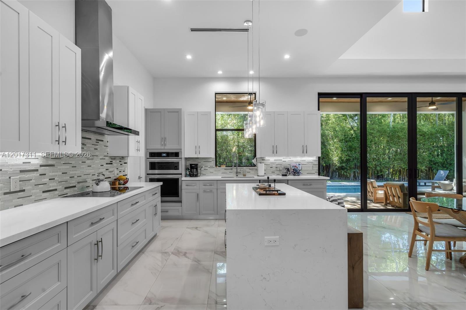 A modern kitchen features light gray cabinetry, white quartz countertops, a central island, and large glass doors — 1010 Genoa St, Coral Gables FL 33134, CORAL GABLES, FL