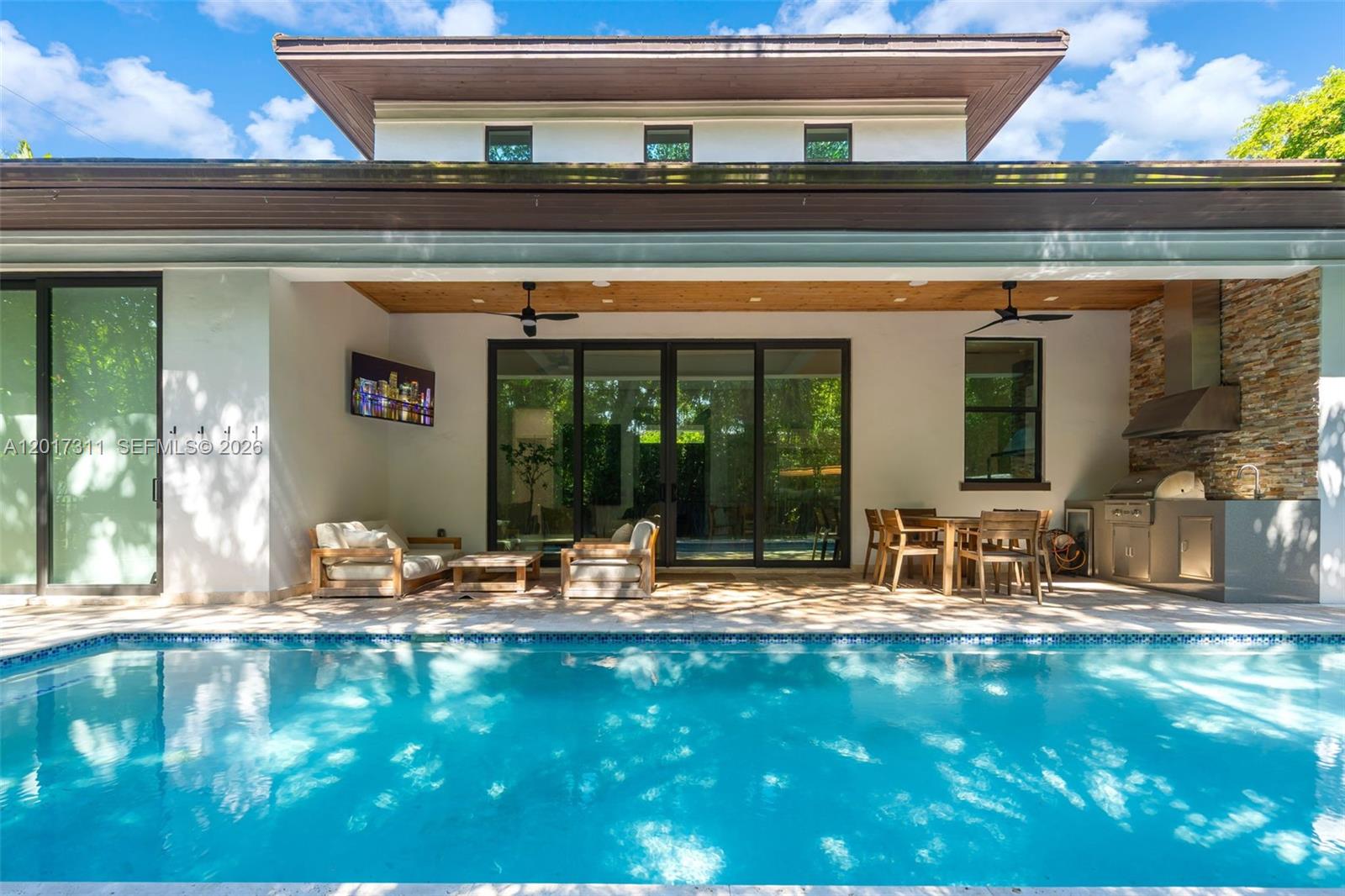 A covered patio with a pool, outdoor kitchen, and seating area overlooks a backyard — 1010 Genoa St, Coral Gables FL 33134, CORAL GABLES, FL