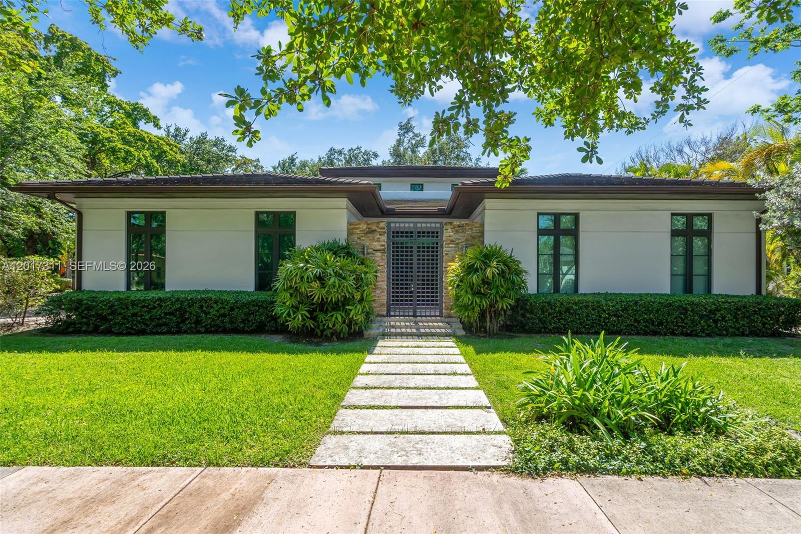 A single-story house features a stone entryway, dark-framed windows, and a stone paver walkway — 1010 Genoa St, Coral Gables FL 33134, CORAL GABLES, FL