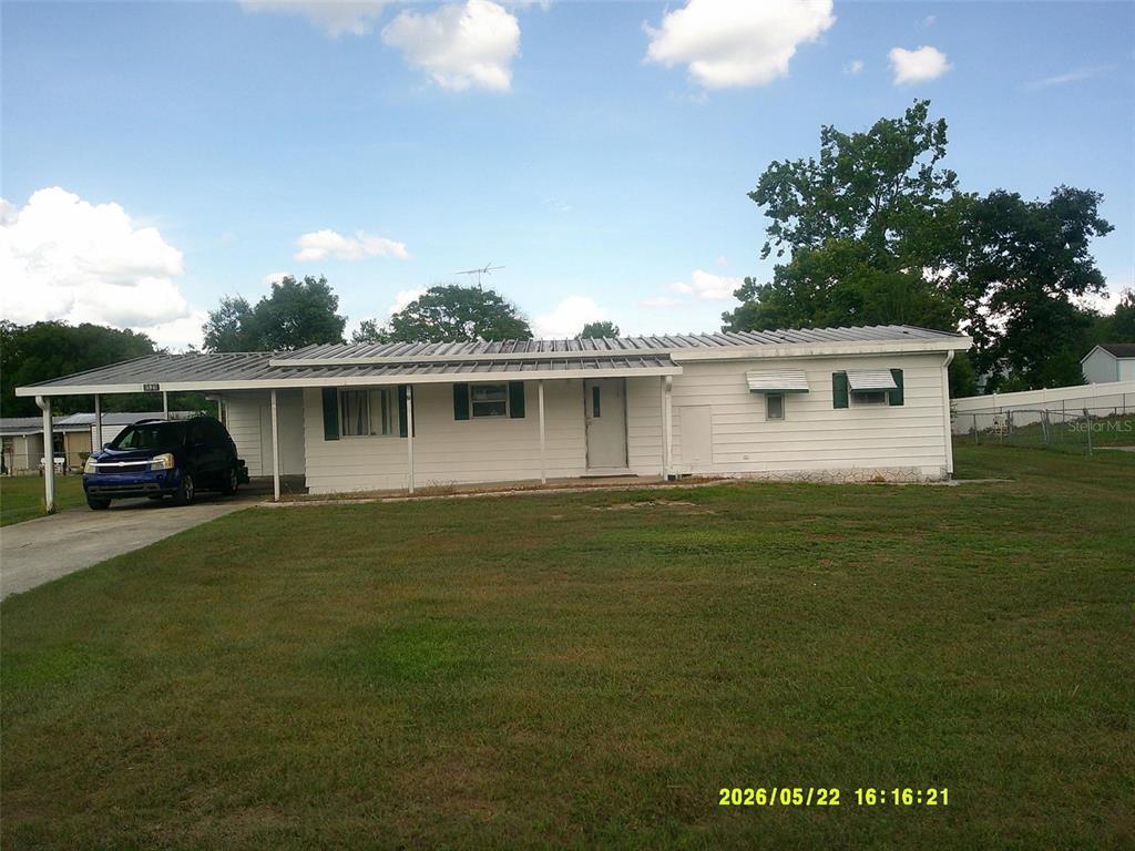 A single-story white house with a metal roof and an attached carport sits on grass — 15211 SE 104TH COURT, SUMMERFIELD, FL