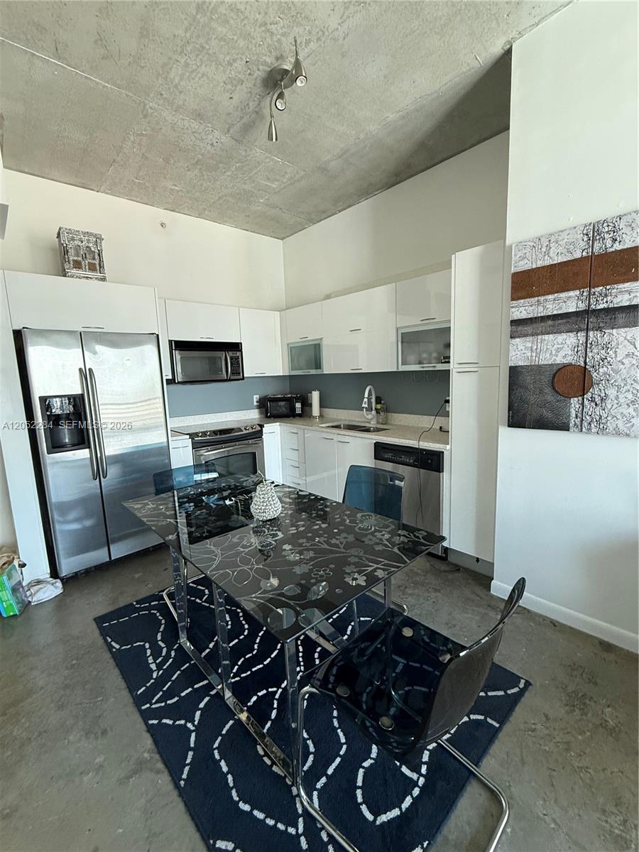 A kitchen features white cabinets, stainless steel appliances, and a dining table on concrete floors — 133 NE 2nd Ave # 2811, Miami FL 33132, MIAMI, FL