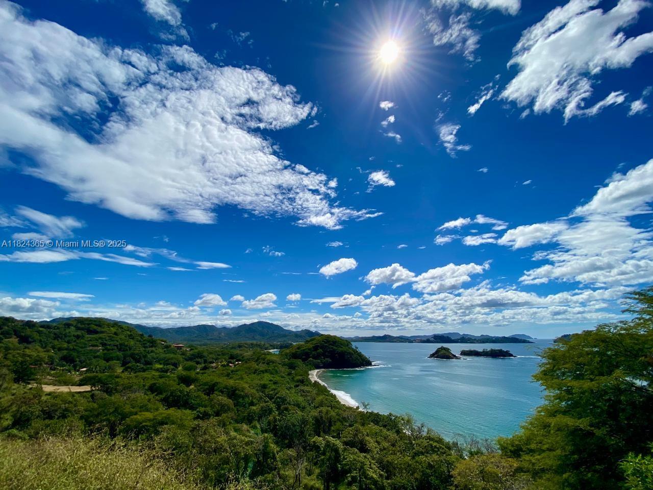 A high-angle view of a tropical coastline with lush green hills, a beach, and islands — 27 de Abril Playa Junquillal, IA 50303, IA