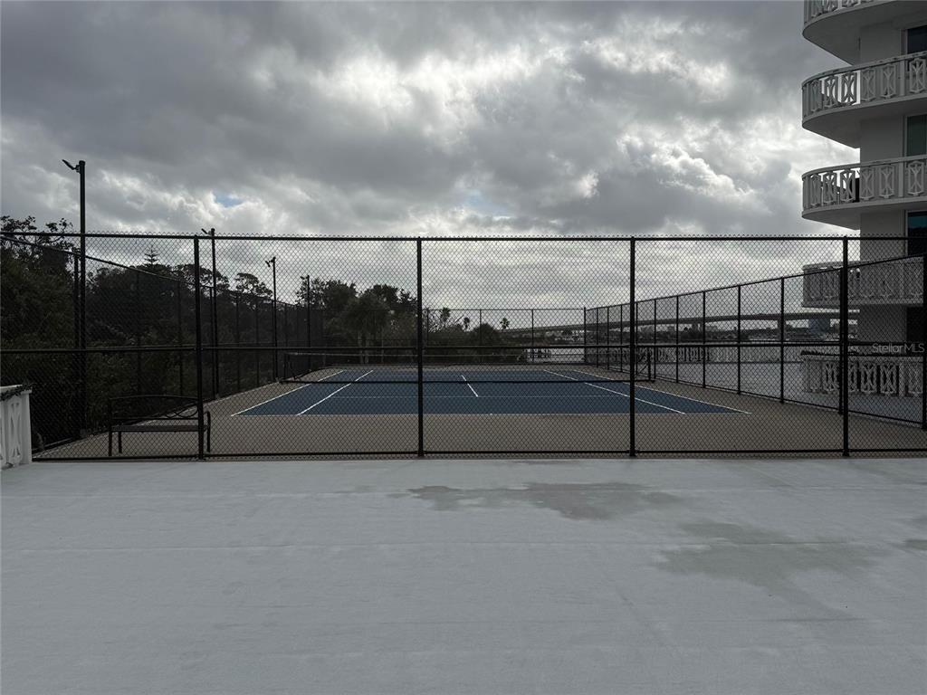 A fenced tennis court sits outdoors next to a multi-story building under a cloudy sky — 925 N HALIFAX AVENUE UNIT 102, DAYTONA BEACH, FL