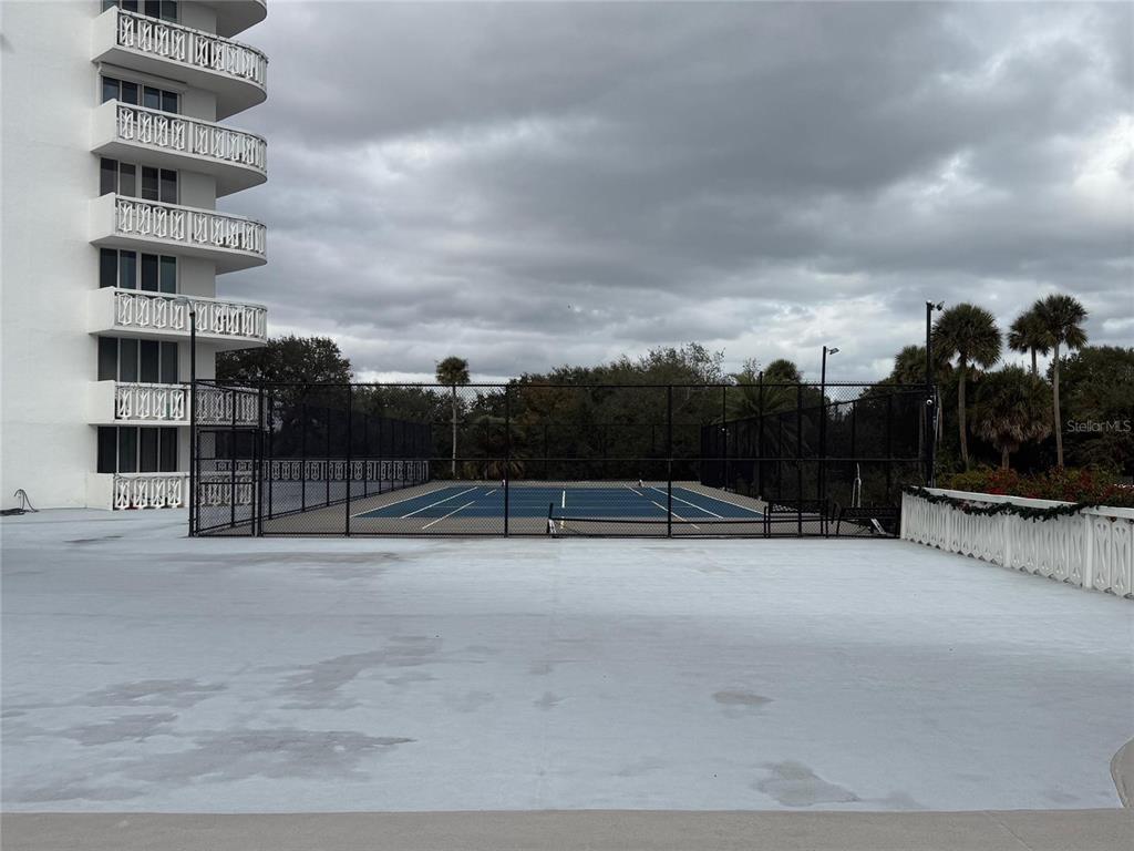 A tennis court is enclosed by a chain-link fence next to a high-rise building — 925 N HALIFAX AVENUE UNIT 102, DAYTONA BEACH, FL