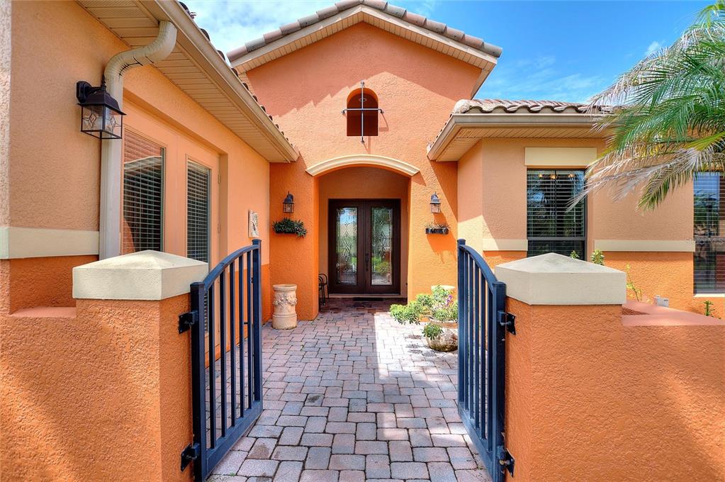 A gated brick courtyard leads to the double front doors of an orange stucco house — 915 SAN RAPHAEL STREET, POINCIANA, FL