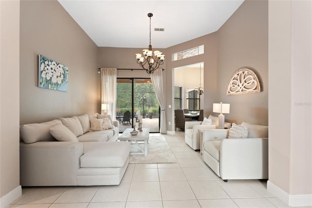 A living room features light-colored furniture, tile flooring, a chandelier, and sliding glass doors — 915 SAN RAPHAEL STREET, POINCIANA, FL