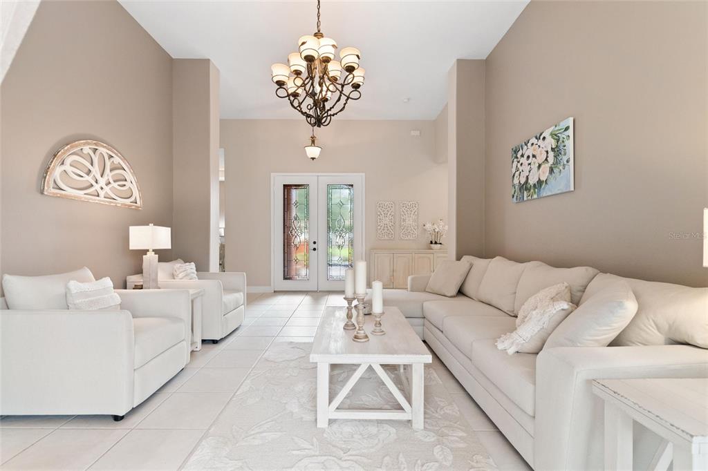 A bright living room features white furniture, a large chandelier, and a light-colored rug — 915 SAN RAPHAEL STREET, POINCIANA, FL