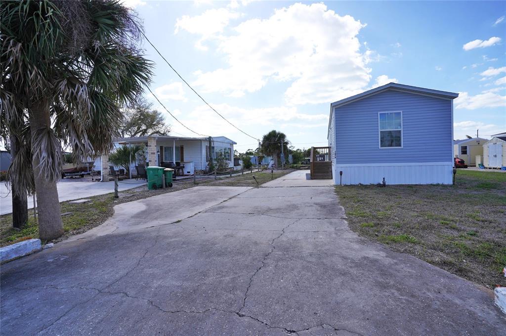 A paved driveway leads between two manufactured homes under a bright, partly cloudy sky — 1276 SEAGULL DRIVE, ENGLEWOOD, FL