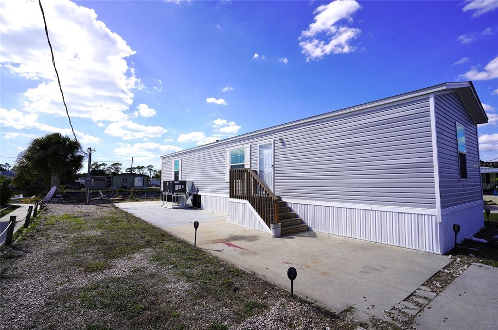 A light gray mobile home features a concrete patio, wooden stairs, and a metal HVAC unit — 1276 SEAGULL DRIVE, ENGLEWOOD, FL