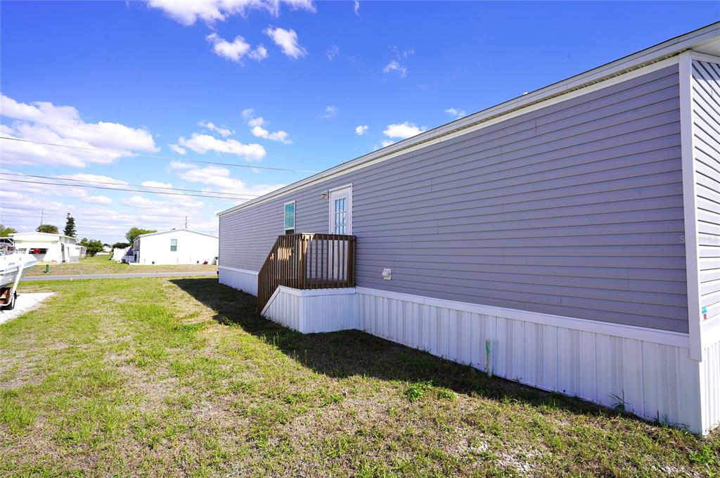 The exterior of a light gray manufactured home features a wooden deck and white skirting — 1276 SEAGULL DRIVE, ENGLEWOOD, FL