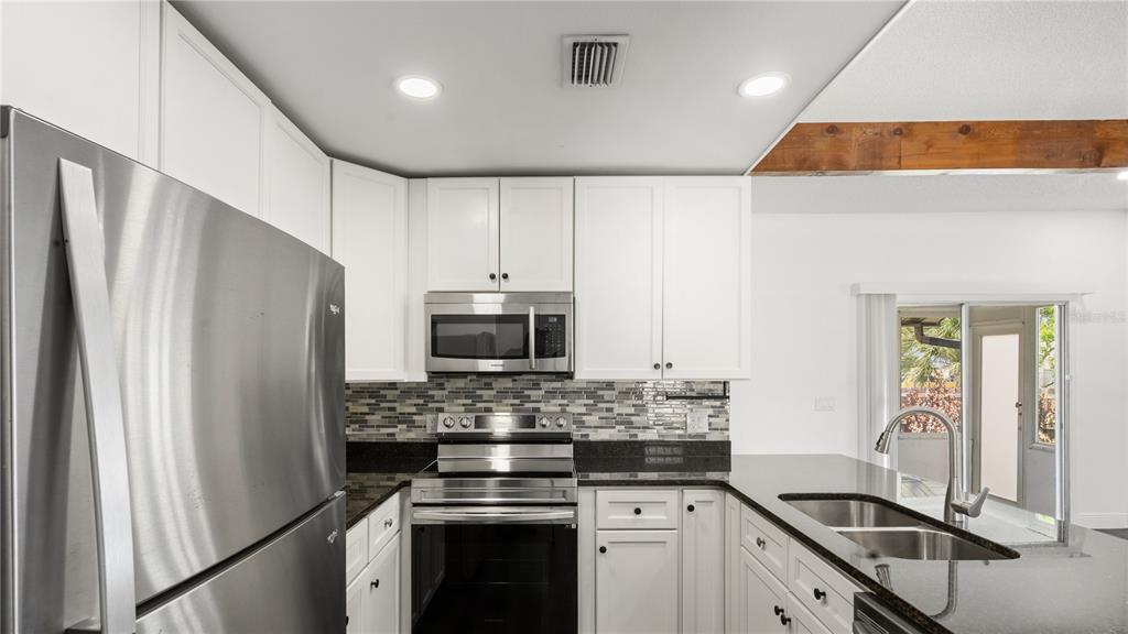 A kitchen features white cabinets, stainless steel appliances, dark countertops, and a tile backsplash — 4999 DOVER CIRCLE, ORLANDO, FL
