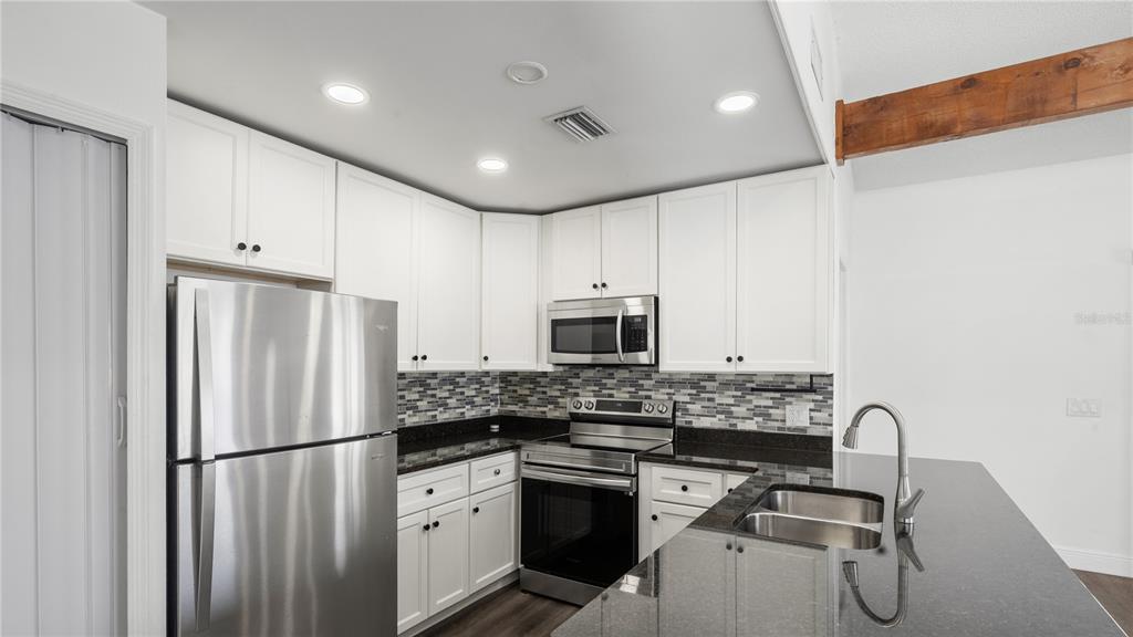 A kitchen with white cabinets, stainless steel appliances, a mosaic backsplash, and dark countertops — 4999 DOVER CIRCLE, ORLANDO, FL