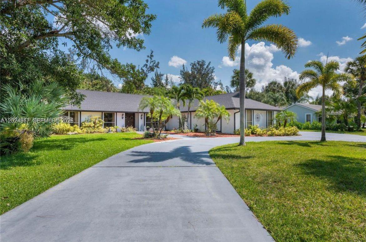 A single-story house with a gray driveway, palm trees, and a green lawn — 13353 Doubletree Cir, Wellington FL 33414, WELLINGTON, FL