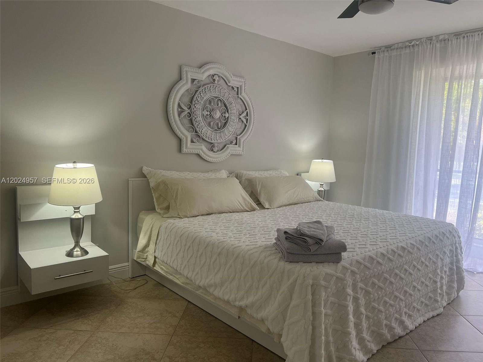 A bedroom features a white bed with a textured cover, wall-mounted nightstands, and decorative wall art — 13353 Doubletree Cir, Wellington FL 33414, WELLINGTON, FL