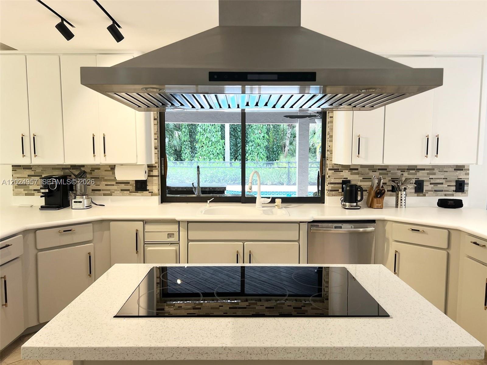 A kitchen features white cabinetry, a central island with a cooktop, and a stainless hood — 13353 Doubletree Cir, Wellington FL 33414, WELLINGTON, FL