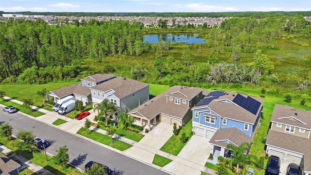 An aerial view shows suburban houses with driveways, solar panels, and a pond in the background — 16448 PARABLE WAY, WINTER GARDEN, FL