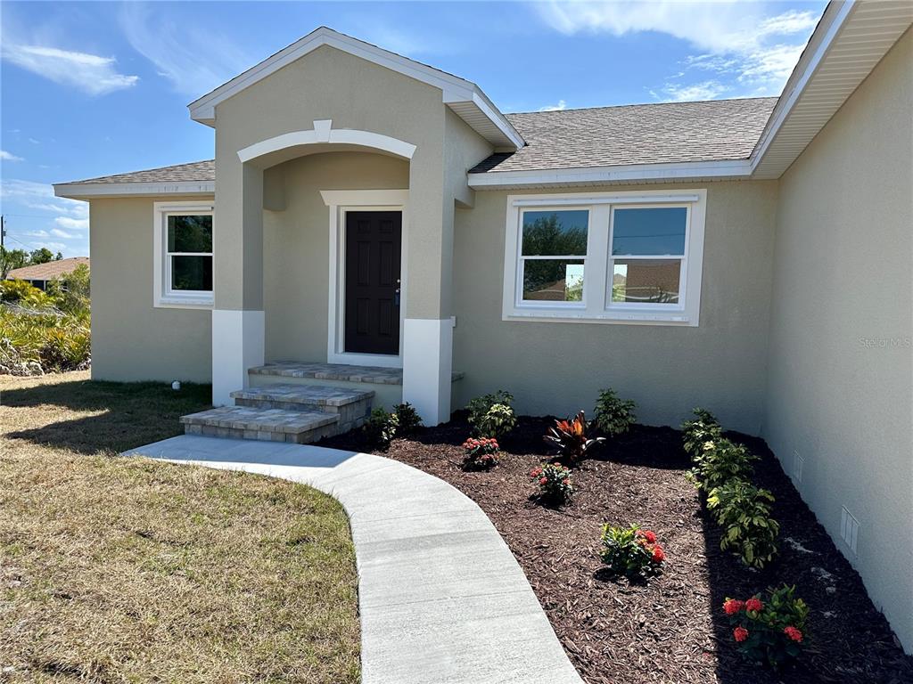 A beige house exterior features a covered entryway, stone steps, and a landscaped front yard — 9172 RAVEL STREET, PORT CHARLOTTE, FL