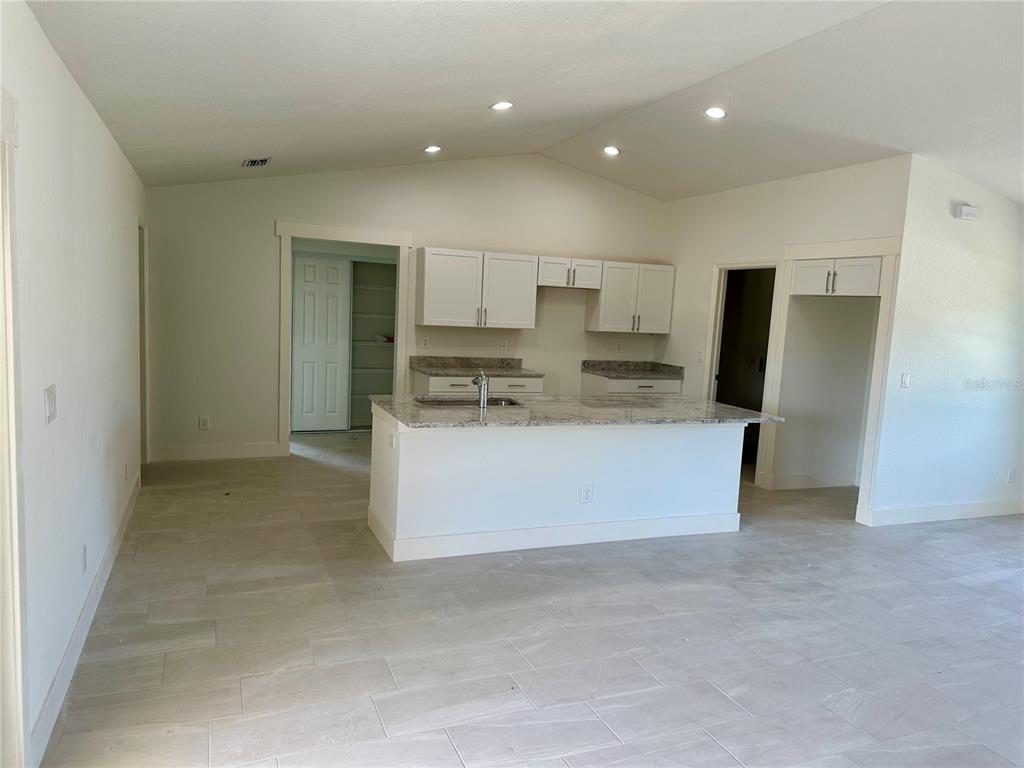 A kitchen with white cabinets, granite countertops, a center island, and light-colored tile flooring — 9172 RAVEL STREET, PORT CHARLOTTE, FL