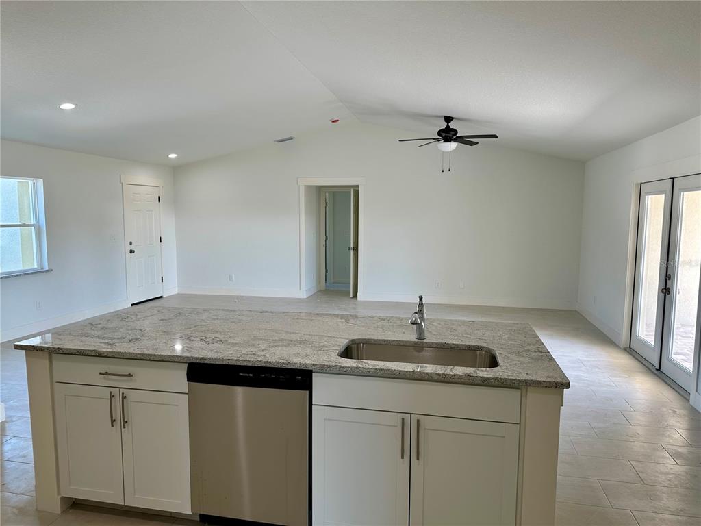 A kitchen island with a stainless steel sink and dishwasher sits in an open-concept room — 9172 RAVEL STREET, PORT CHARLOTTE, FL