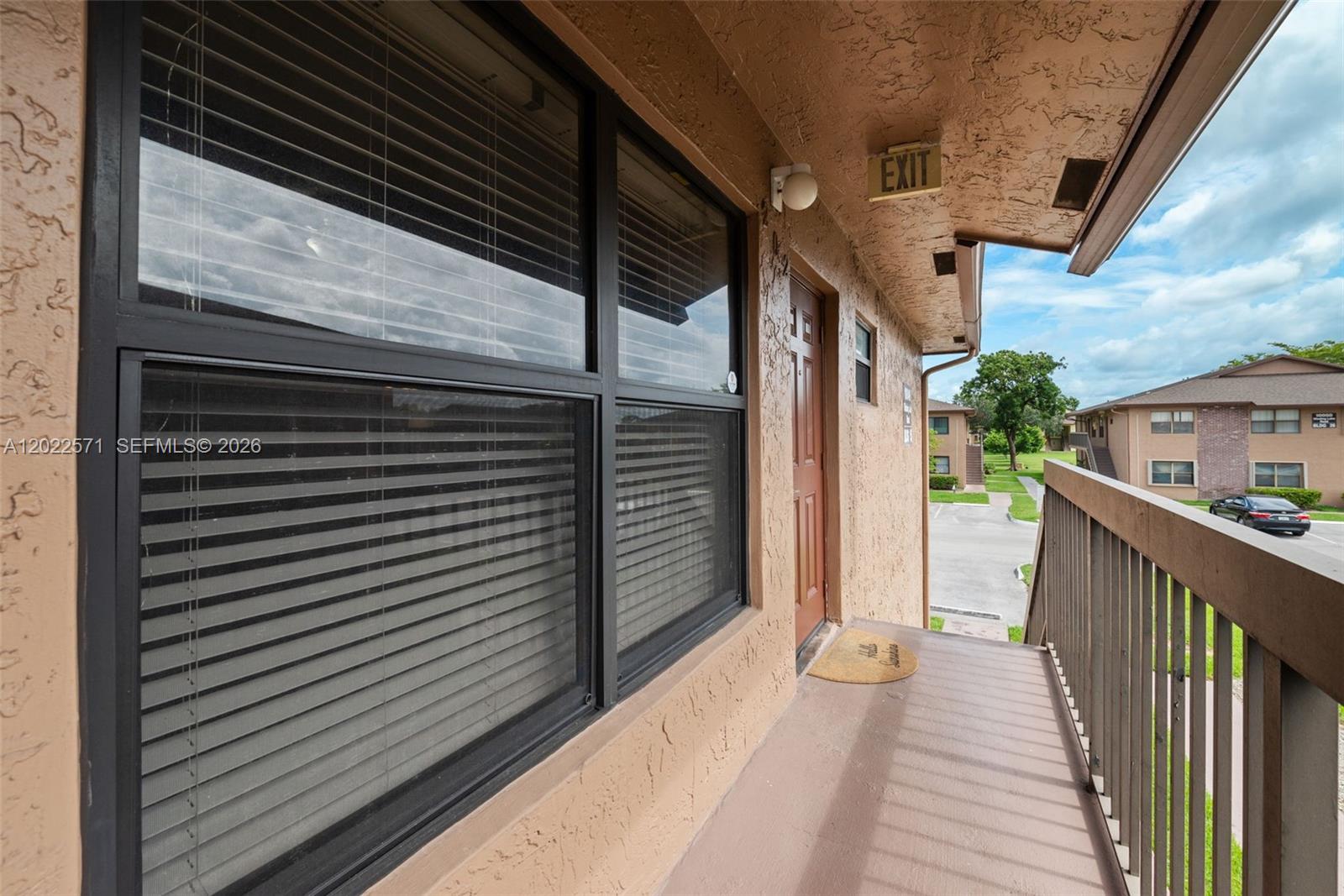 An exterior walkway features a brown door, a window with blinds, and a wooden railing — 10049 Winding Lake Rd # 202, Sunrise FL 33351, SUNRISE, FL