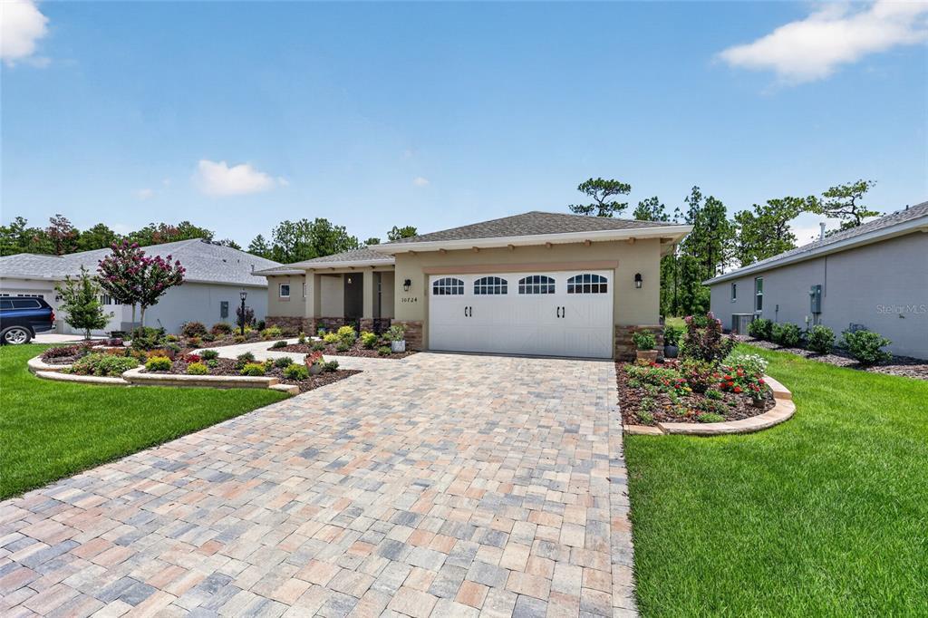 A single-story house with a paved driveway, a two-car garage, and landscaped front garden beds — 10724 SW 101ST LOOP, OCALA, FL