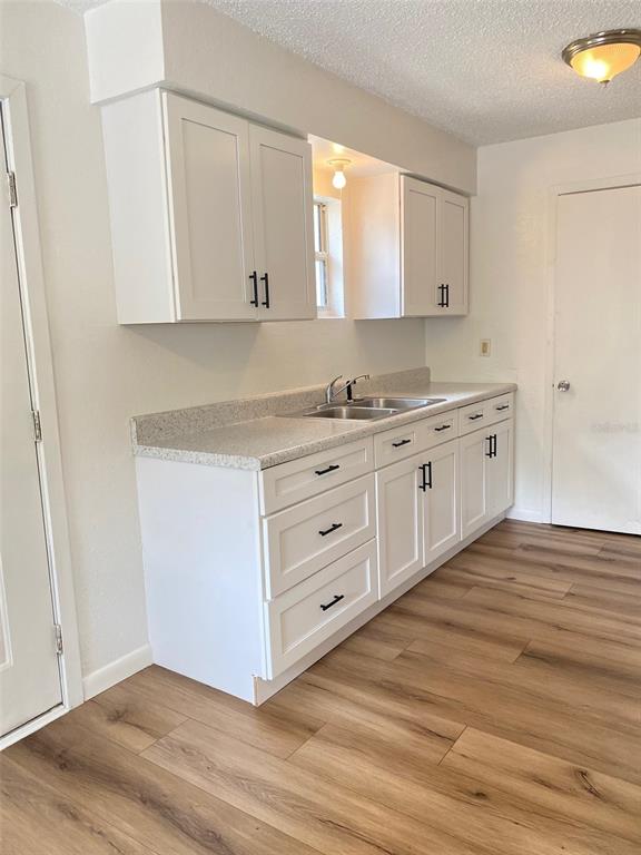 A kitchen features white cabinets, a speckled countertop, and light wood-look flooring — 205 NE 147 STREET, CROSS CITY, FL