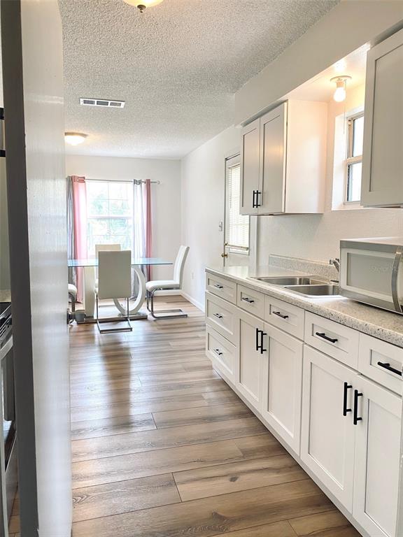 A kitchen with white cabinets and light wood-look flooring opens into a dining area — 205 NE 147 STREET, CROSS CITY, FL