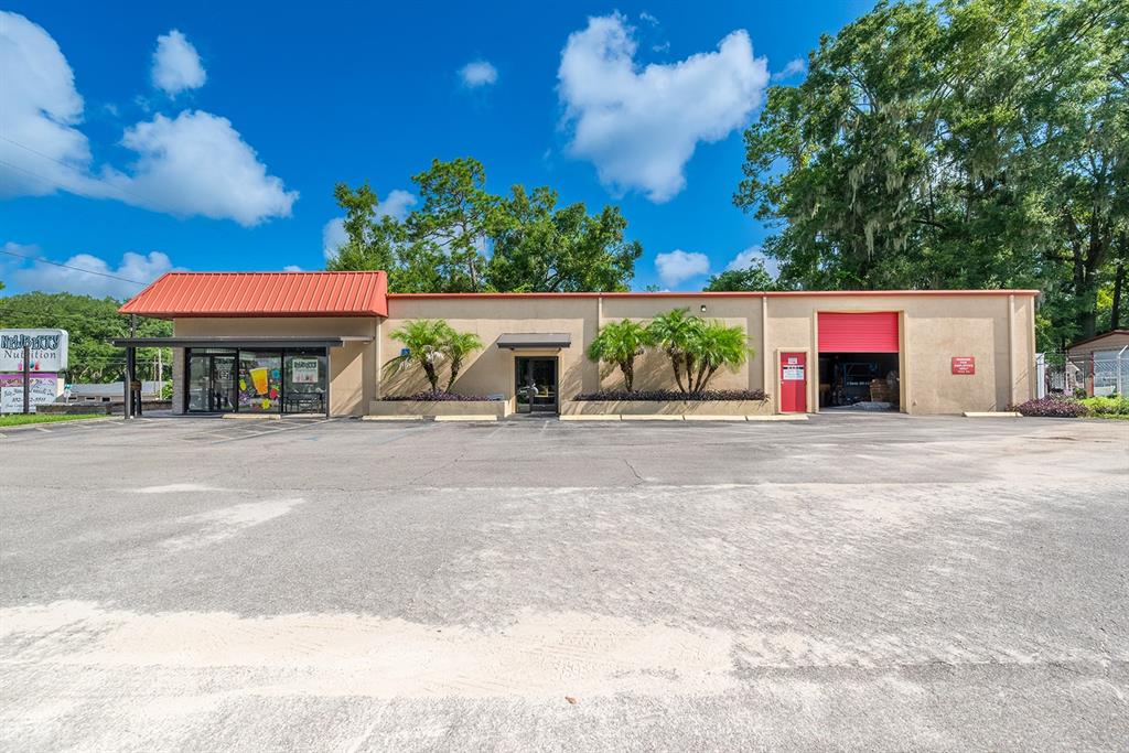 A single-story commercial building with a red metal roof, parking lot, and palm trees — 305 SW 250TH STREET, NEWBERRY, FL