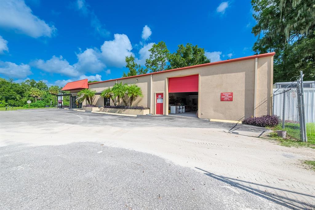 A tan commercial building with a red roll-up door and a paved parking lot — 305 SW 250TH STREET, NEWBERRY, FL