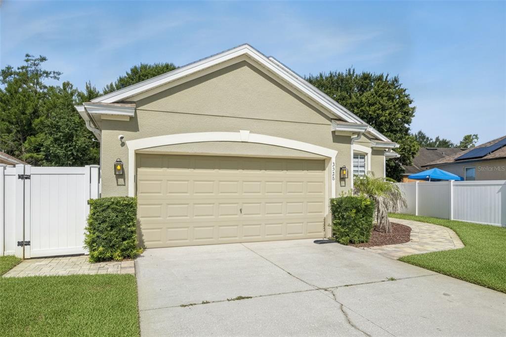 A beige house exterior features a two-car garage, a white vinyl fence, and a walkway — 3528 BERKSHIRE WOODS TERRACE, DELTONA, FL