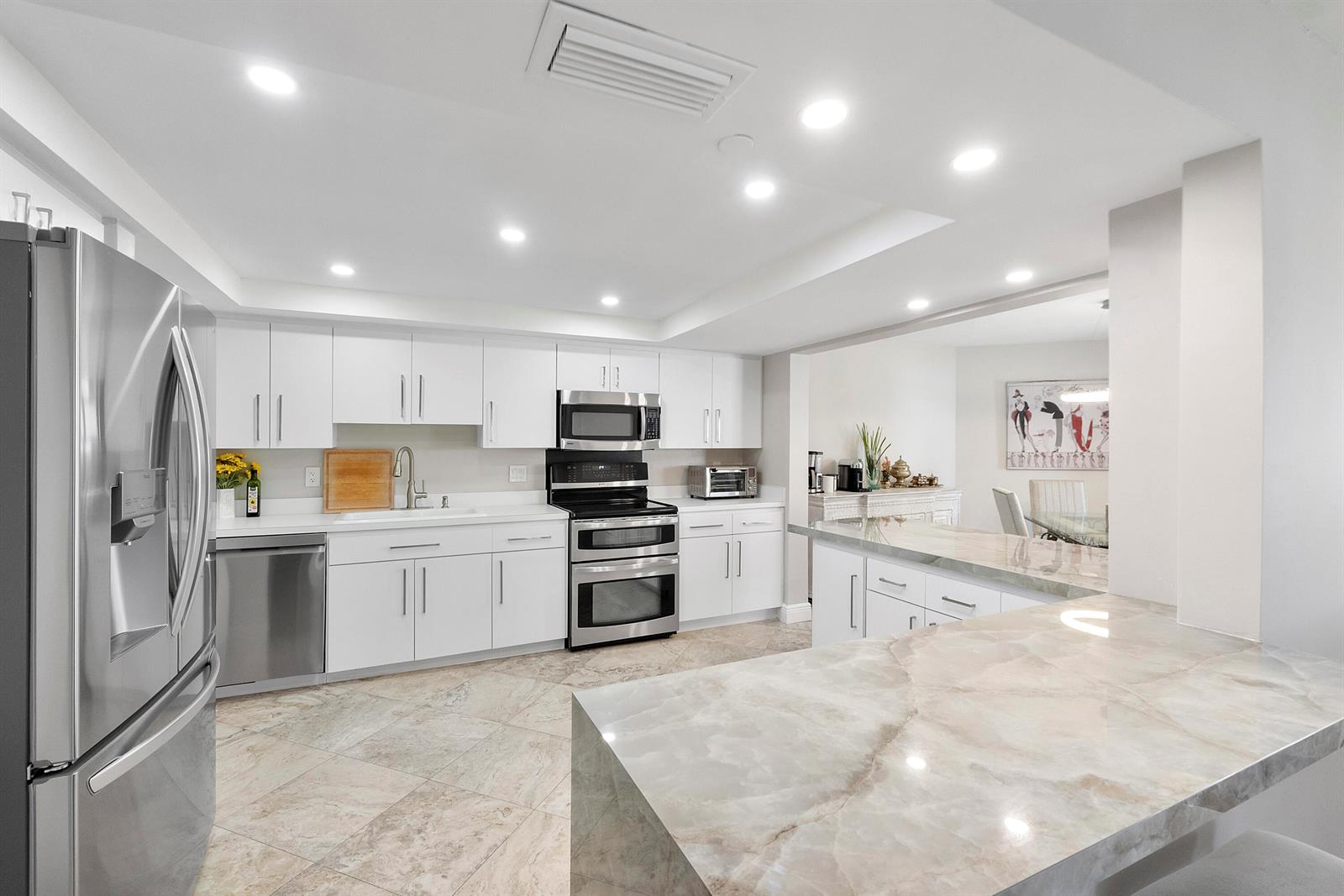 A modern kitchen features white cabinets, stainless steel appliances, and a marble-topped breakfast bar — 501 N Riverside Drive # 203, Pompano Beach FL 33062, POMPANO BEACH, FL