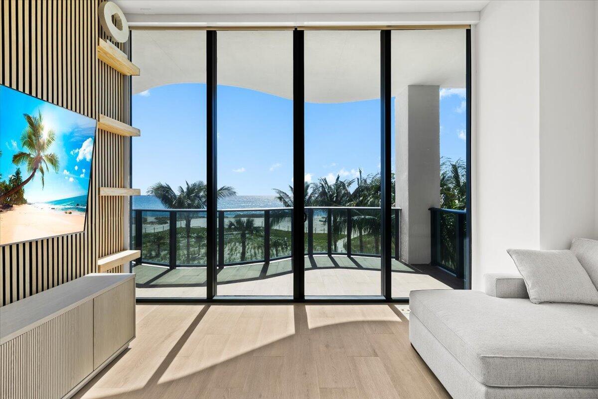 A modern living room features wood-slat walls, a large television, and floor-to-ceiling windows overlooking the ocean — 900 N Ocean Boulevard # 305, Pompano Beach FL 33062, POMPANO BEACH, FL