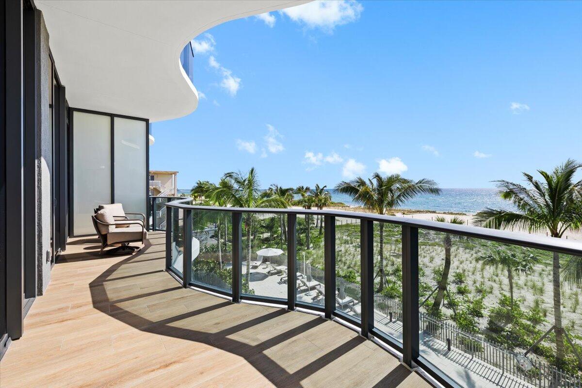 A curved balcony with wood-look tile flooring overlooks a sandy beach and the ocean — 900 N Ocean Boulevard # 305, Pompano Beach FL 33062, POMPANO BEACH, FL