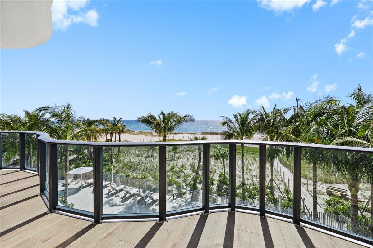 A curved balcony with glass railings overlooks a sandy beach, palm trees, and the ocean — 900 N Ocean Boulevard # 305, Pompano Beach FL 33062, POMPANO BEACH, FL