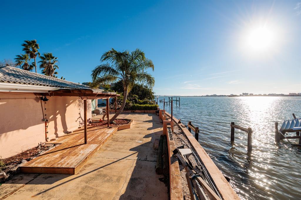 A waterfront patio with a wooden deck, a palm tree, and a concrete seawall — 1844 VENETIAN POINT DRIVE, CLEARWATER, FL