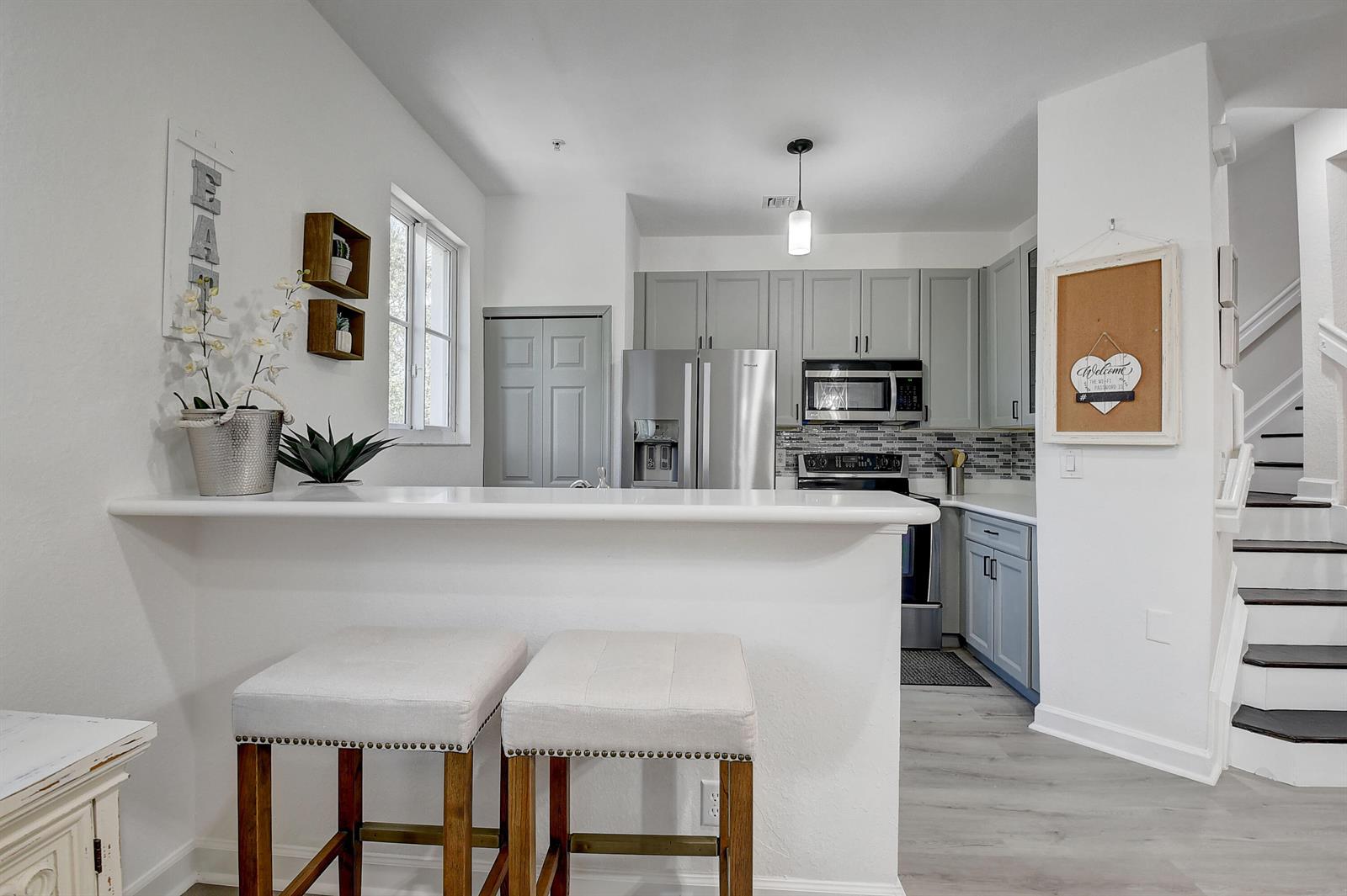 A kitchen with grey cabinets, stainless steel appliances, and a breakfast bar with two stools — 525 Bayfront Drive, Boynton Beach FL 33435, BOYNTON BEACH, FL