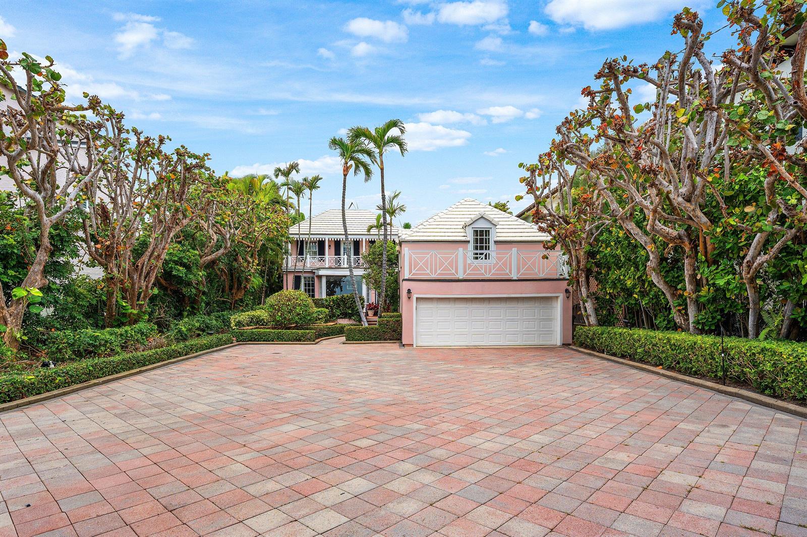 A pink two-story house with a large paved driveway and surrounding trees under a blue sky — 406 N Ocean Boulevard, Delray Beach FL 33483, DELRAY BEACH, FL