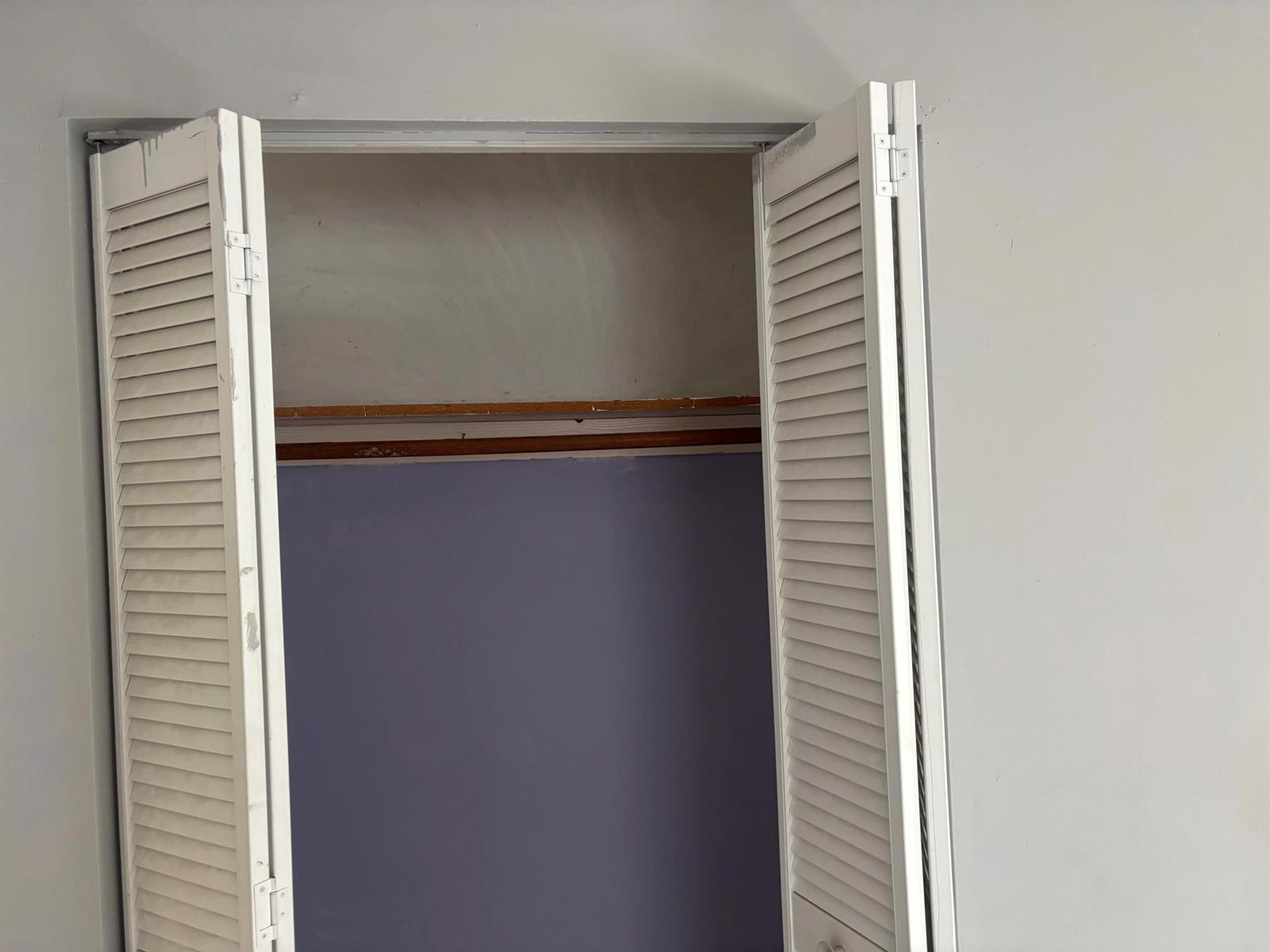 An open closet with white louvered doors, a wooden shelf, and purple interior walls — 1250 SW 5TH Terrace, Deerfield Beach FL 33441, DEERFIELD BEACH, FL